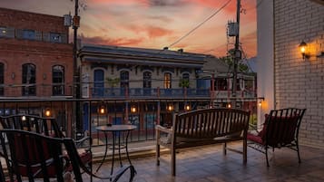 A terrace with outdoor seating, a view of a building with a blue facade, and a sunset sky.
