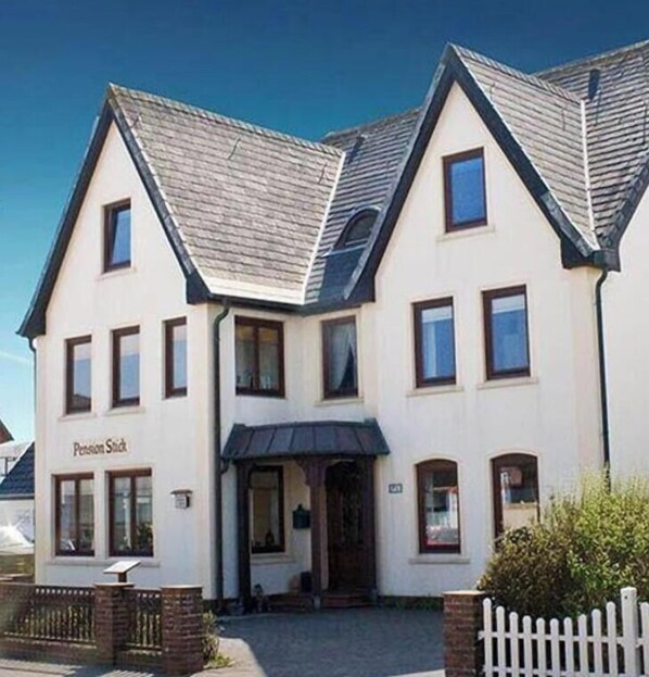A two-story building with a gabled roof, a front entrance, and a sign that reads 'Pension Stuck'. - Single room close to the beach in a quiet location in Wenningstedt - Pension La Mer - (Wenningstedt-Braderup (Sylt))