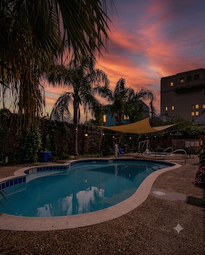 A swimming pool with a curved edge, surrounded by palm trees and a building in the background. - Stylish 2BR Frenchmen Street stay with shared pool, and easy walk to the French Quarter. (New Orleans)