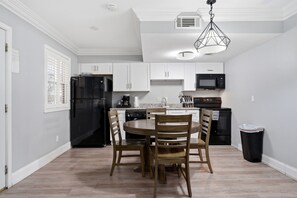 A modern kitchen with white cabinets, a black refrigerator, a microwave, and a dining table with chairs. - Stylish 1BR stay near Frenchmen Street with shared pool, hot tub, and easy walk to the French Quarter. (New Orleans)
