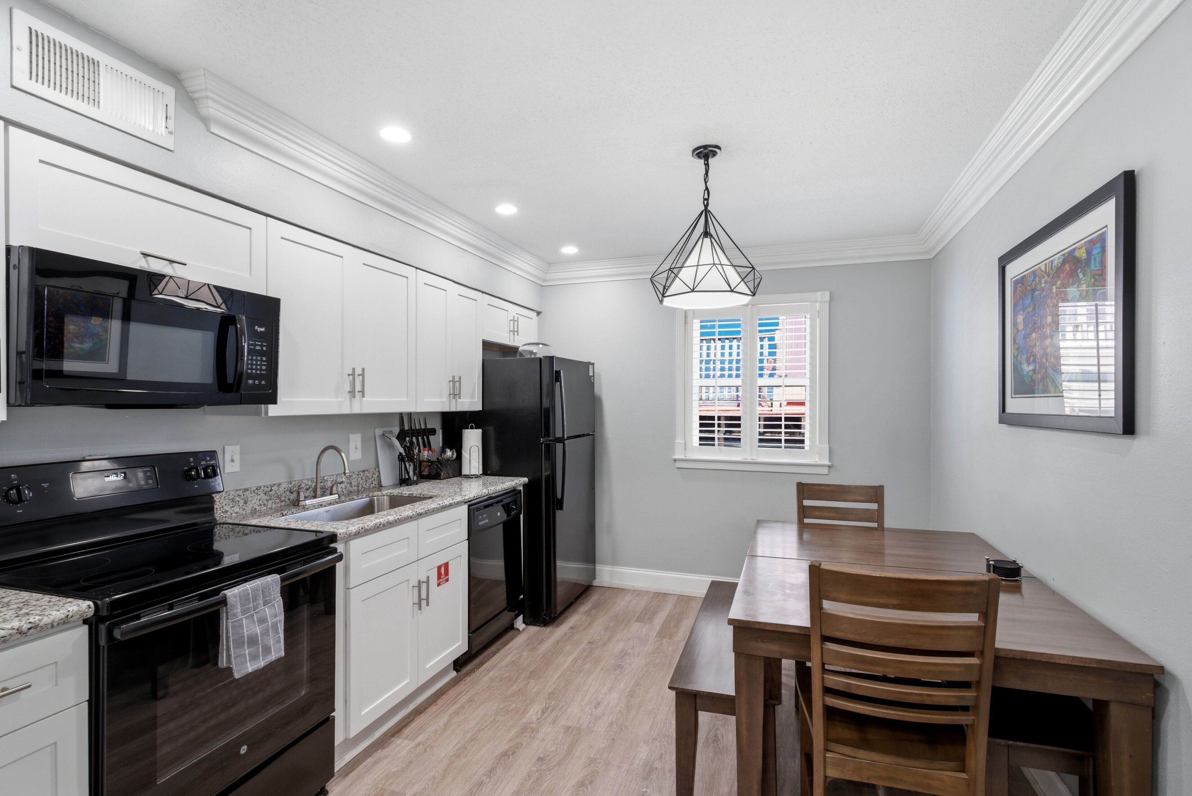 Una cocina moderna con armarios blancos, un microondas negro, un refrigerador negro y una mesa de comedor de madera.