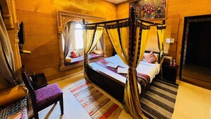 A room with a four-poster bed, a chair, a small table, and a decorative wall piece. - Hotel Unique Heritage  (Jaisalmer)