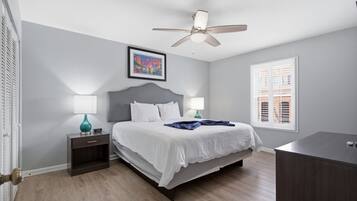 A bedroom with a bed, two bedside tables, a ceiling fan, a window with blinds, and a framed picture on the wall.