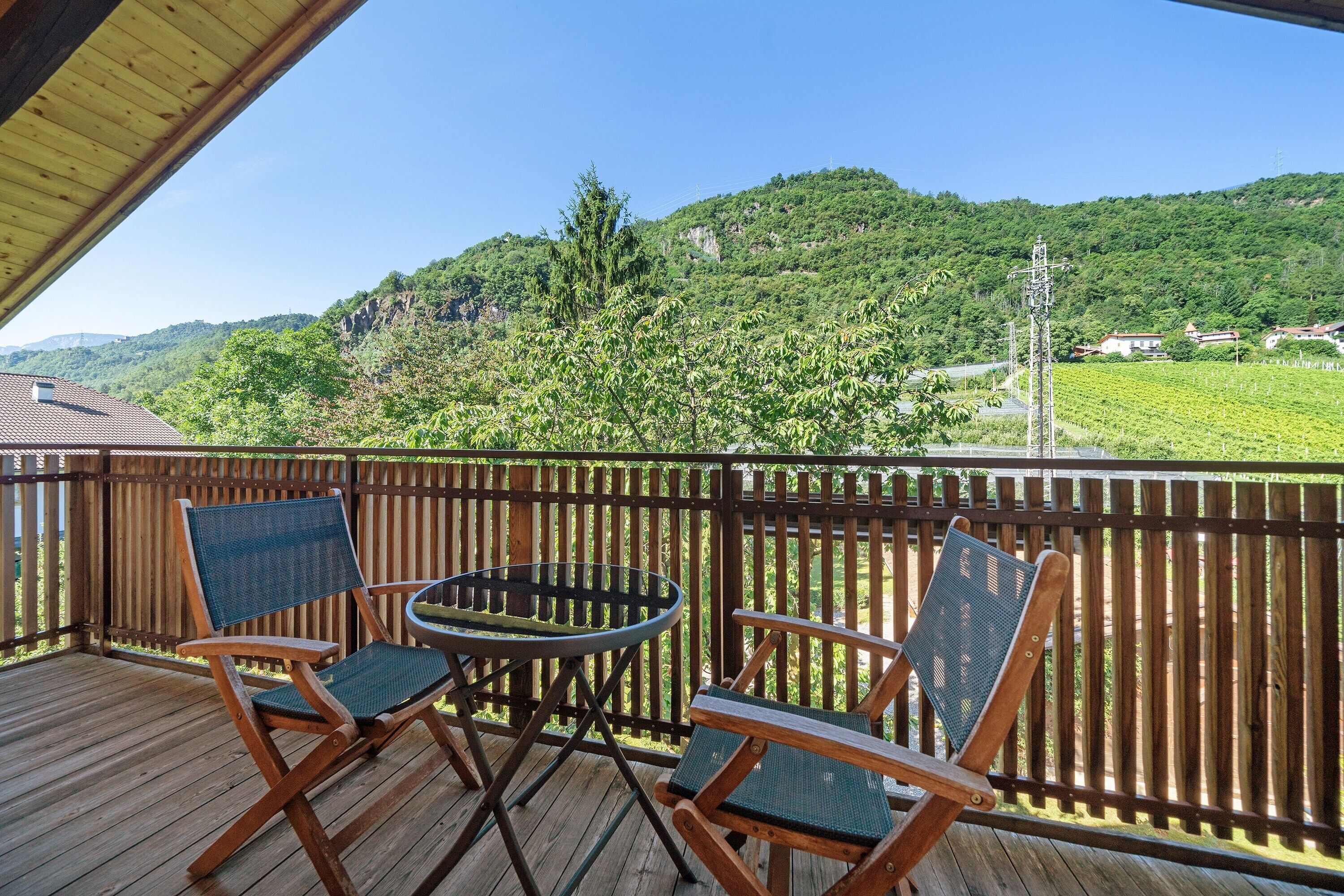 A wooden deck with two folding chairs and a small table, overlooking a lush green hillside.