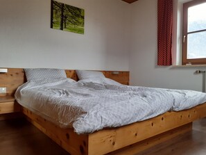 Un letto di legno con copria letto, un comodino, una finestra con tende e un quadro appeso al muro.