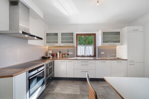 A modern kitchen with a built-in oven, a coffee maker, and a window with a view of greenery. - Zirbentraum – Holiday Apartment with Garden in Lana, South Tyrol (Lana)