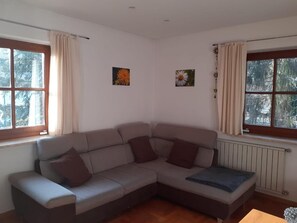 Una stanza d'angolo con un divano angolare grigio, due finestre con tende e due dipinti di fiori appesi al muro.