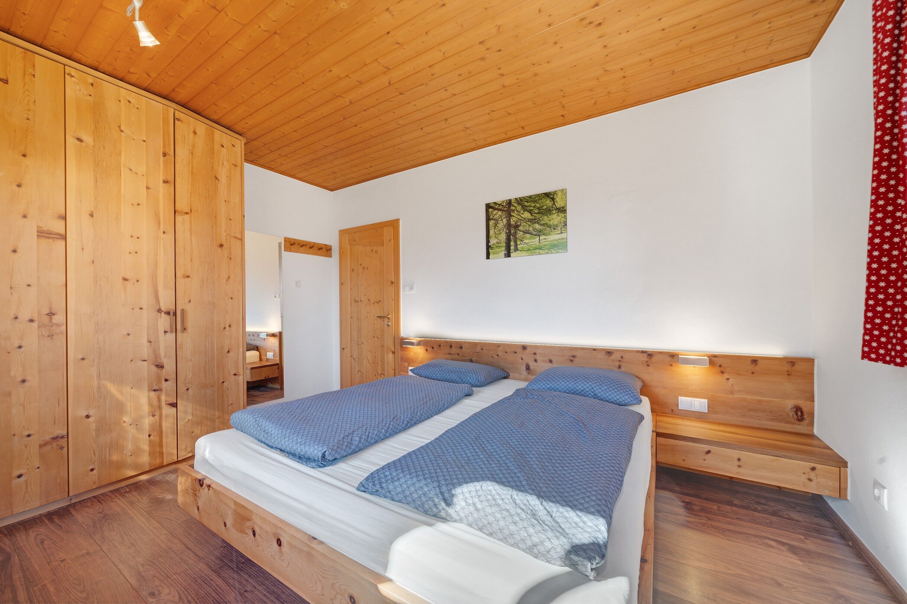 Una camera da letto con soffitto in legno, un letto con biancheria azzurra, un comodino e una lampada a parete.