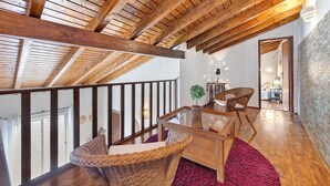 Eine Holzbalkendecke, ein Korbstuhl, ein kleiner Tisch und ein roter Teppich.