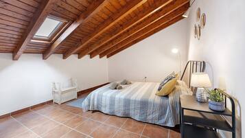 A bedroom with a sloped ceiling, a skylight, a bed with a striped bedspread, a bedside table with a lamp, and a small potted plant.