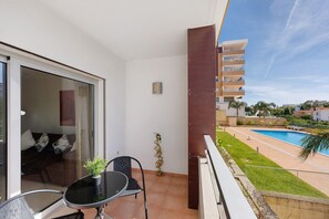 Un balcón con mesa y sillas, una planta en maceta y vistas a una piscina y follaje.