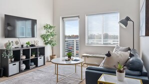 Ett modernt vardagsrum med en platt-TV, ett runt soffbord, en soffa, en golvlampa, en bokhylla och en krukväxt.