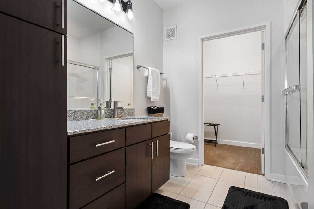 Une salle de bain moderne avec un meuble-lavabo en bois foncé, un grand miroir et un espace douche.
