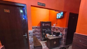 A reception area with a reception desk, a television, a brown cushioned bench, and a door labeled 'Reception'. - Deepak Guest House (Mathura)