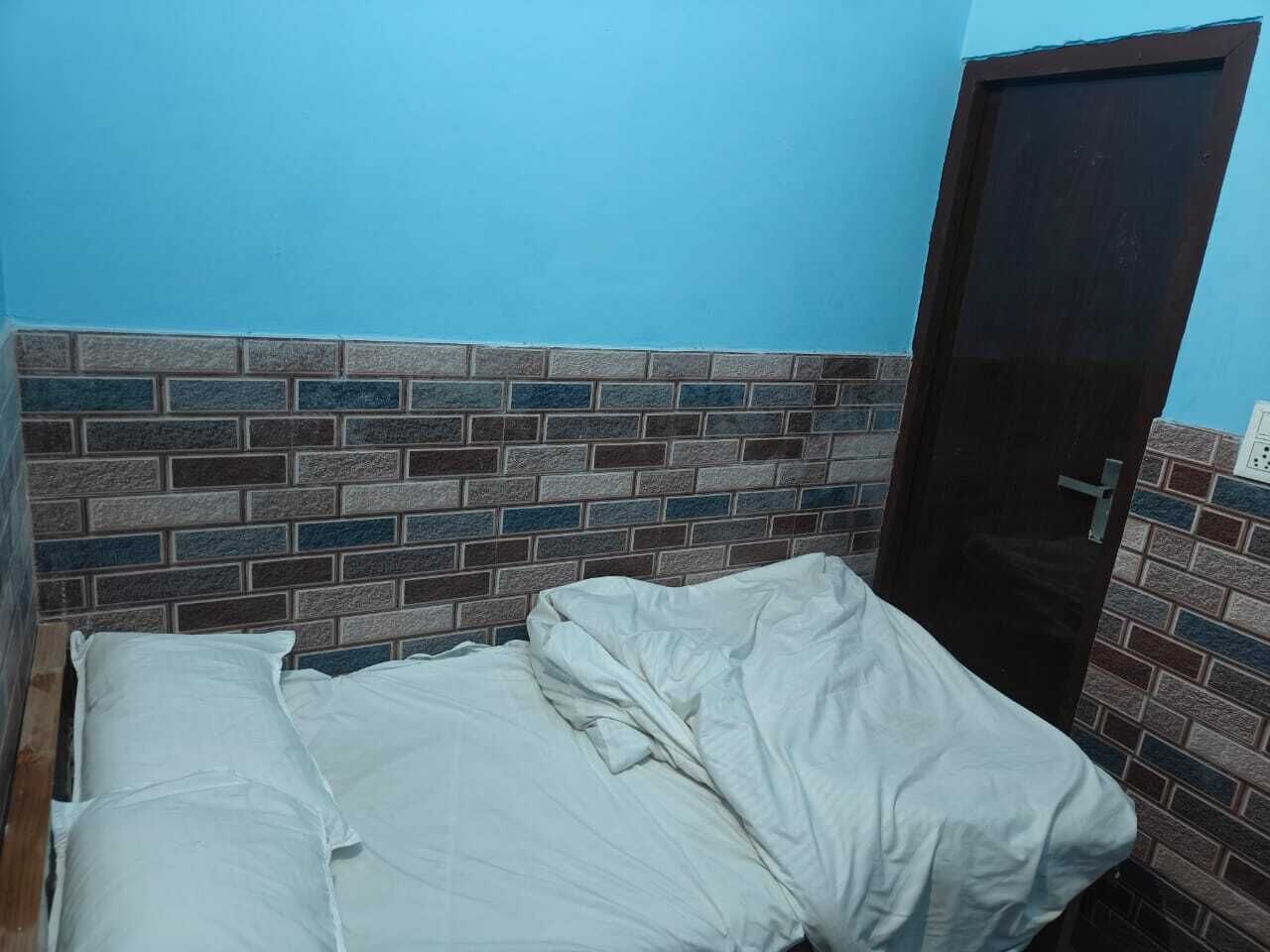 A single bed with white bedding in a room with a brick-patterned headboard and a dark wooden door.