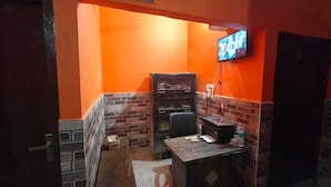 A reception area with a TV mounted on the wall, a desk with a computer, and a bench. - Deepak Guest House (Mathura)
