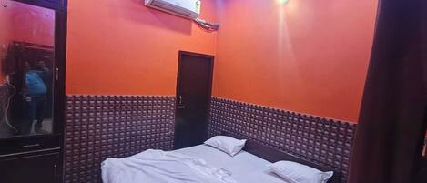 A room with an air conditioning unit, a bed with white bedding, and a door.