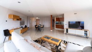Ein modernes Wohnzimmer mit Sofa, Couchtisch, Fernseher und einem Essbereich mit Stühlen und Tisch.