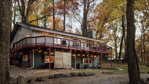 A two-story cabin with a balcony, surrounded by trees with autumn foliage. - Huckleberry Hills | Hot Tub & Fire Pit & Dogs (Harpers Ferry)