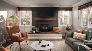 A living room with a fireplace, a sofa, a chair, a coffee table, and a TV mounted on the wall. - Huckleberry Hills | Hot Tub & Fire Pit & Dogs (Harpers Ferry)