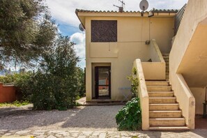 Un bâtiment doté d’un escalier en pierre menant à une porte, le tout entouré de verdure.