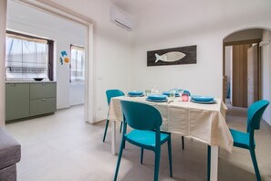 Un coin repas avec une table dressée pour quatre personnes, des chaises de couleur turquoise et un élément de décoration murale en forme de poisson.