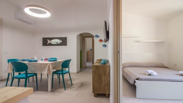 A room with a bed, a table with chairs, a TV, and a fish decoration on the wall. - GuestHost - Cozy and bright 70 square meters apartment, perfect for four people, located on the first floor of a building without an elevator.The property enjoys an excellent location, in an extremely quiet area and just 250 meters from the seafront. Ame (Cannigione)