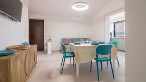 A dining area with a table set for four, teal chairs, a wooden buffet, and a TV mounted on the wall. - GuestHost - Cozy and bright 70 square meters apartment, perfect for four people, located on the first floor of a building without an elevator.The property enjoys an excellent location, in an extremely quiet area and just 250 meters from the seafront. Ame (Cannigione)