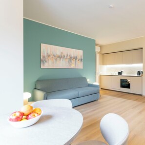 Ein modernes Wohnzimmer mit einer Couch, einem Esstisch mit Früchten und einer Küche im Hintergrund.