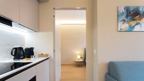 Ett modernt kök med en kaffebryggare, ett litet bord med en lampa och en soffa i en hall som leder till ett vardagsrum.