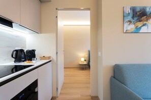 Eine moderne Küche mit Kaffeemaschine, einem kleinen Tisch mit Lampe und einer Couch in einem Flur, der in einen Wohnbereich führt.