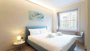 Ett modernt hotellrum med en säng, ett sängbord, en lampa och en tavla på väggen.