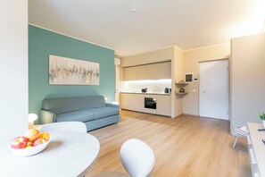 A modern living room with a sofa, a dining table with fruit, and a kitchen area with a fridge and oven. - Arco della Pace Sweet Home B by Halldis (Milan)