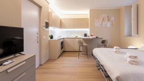 Kompakti hotellihuone, jossa on pieni keittiönurkkaus, sänky, televisio ja työpöytä.