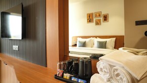 Habitación de hotel con cama, televisor montado en la pared, bandeja con artículos de aseo y un espejo que refleja la habitación.