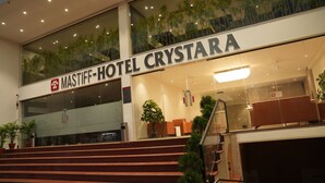 Entrada de hotel con una escalera que conduce al vestíbulo, fachada de vidrio y plantas de interior.