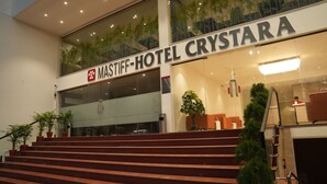 Entrada de un hotel con un cartel que dice 'MASTIFF-HOTEL CRYSTARA', una escalera y plantas en macetas.