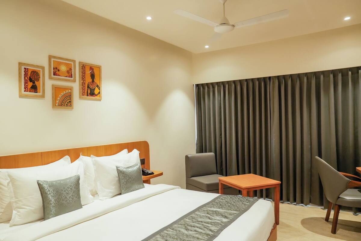 Una habitación de hotel con cama, escritorio, silla y un ventanal con cortinas.