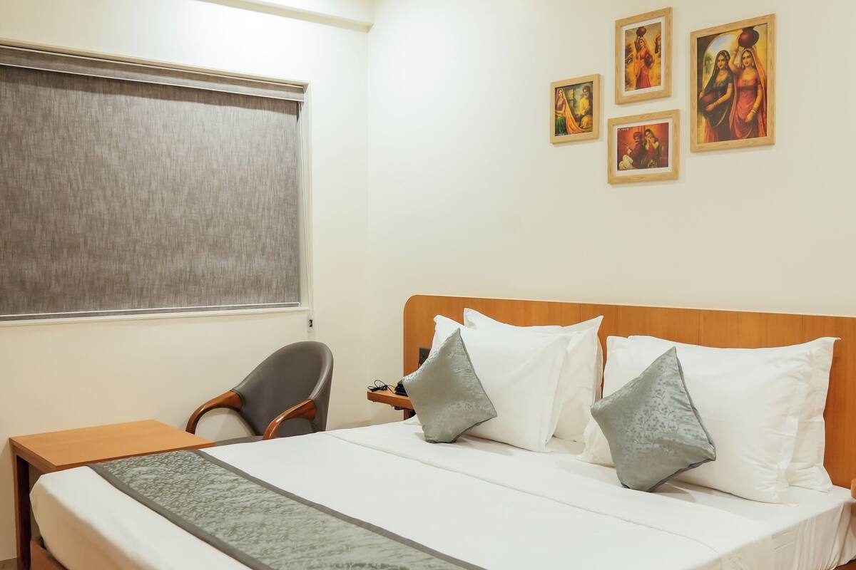 Una habitación de hotel con cama, escritorio, silla, ventilador de techo y obras de arte en la pared.