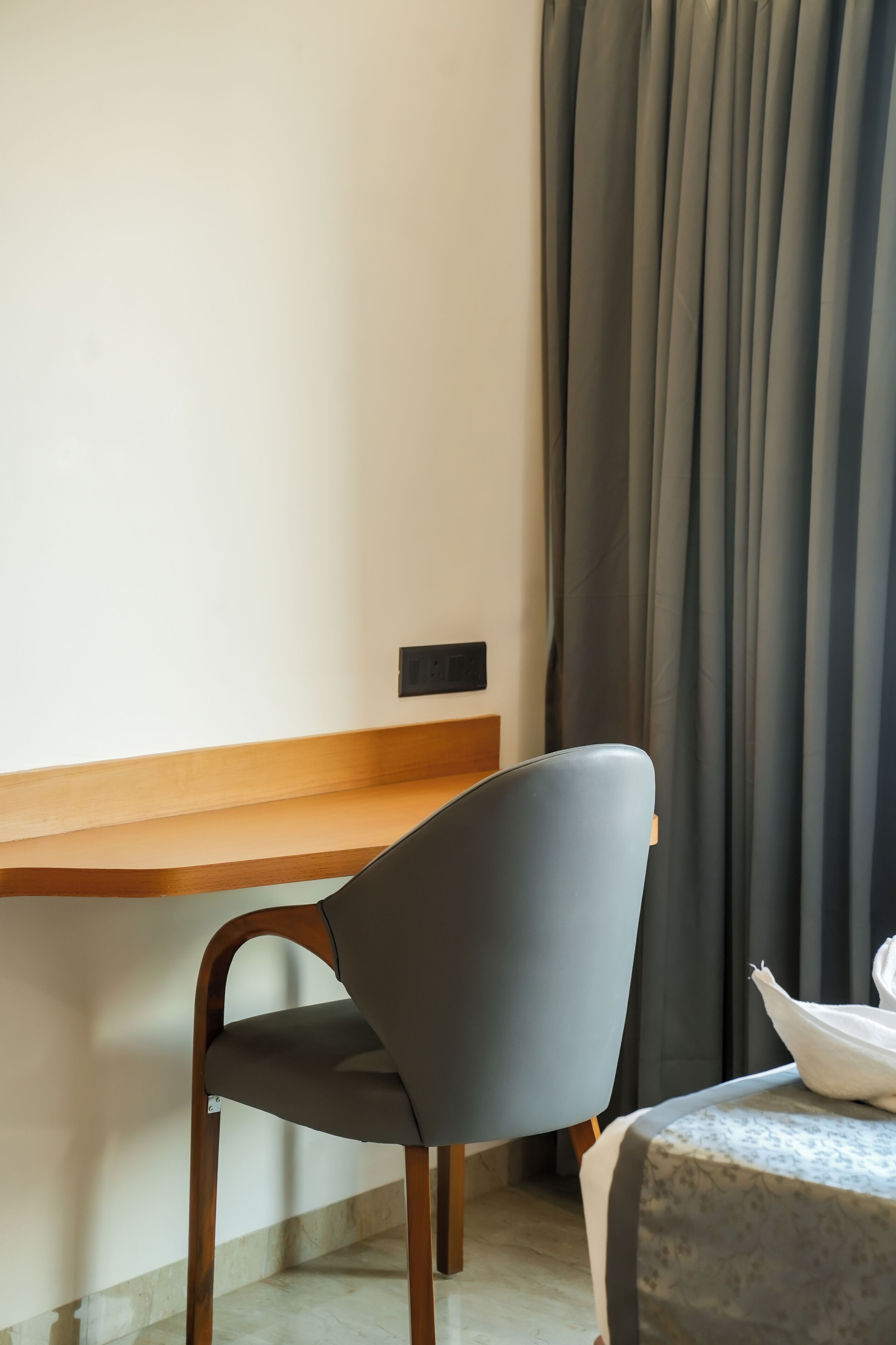 Una silla con asiento oscuro y patas de madera, una mesa de madera y una cortina.