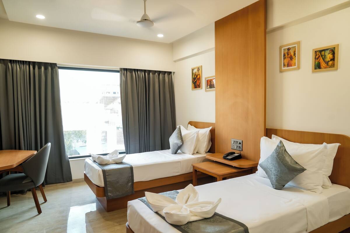 Habitación de hotel con dos camas, un escritorio, una silla, una mesita y una ventana con cortinas.