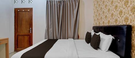 Habitación de hotel con una cama, una puerta de madera, una cortina y un papel tapiz estampado.