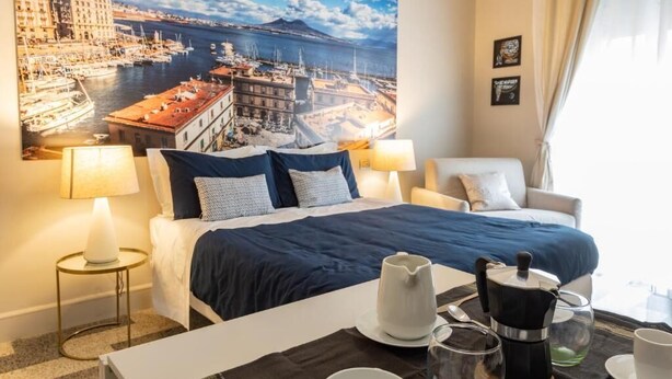 A hotel room with a bed, a coffee table with tea set, a chair, and a large cityscape painting on the wall.