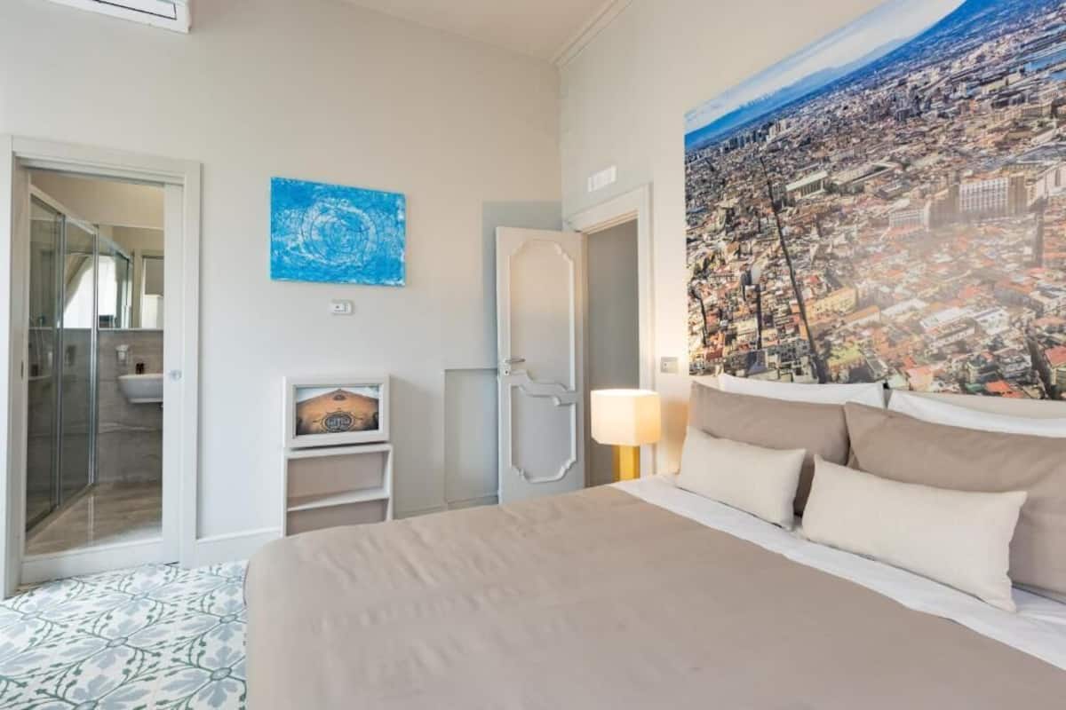 Ett hotellrum med en säng, en tavla, ett badrum och utsikt över staden.