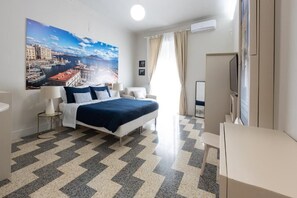 A hotel room with a bed, bedside tables, a TV, a large window with curtains, and a cityscape painting on the wall. - I 4 Elementi  (Naples)