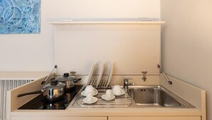 A compact kitchenette with a stove, pots, a sink, and a dish rack.