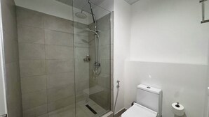 Kylpyhuoneessa on lasiseinällä varustettu suihku, wc ja valkoinen pesuallas.