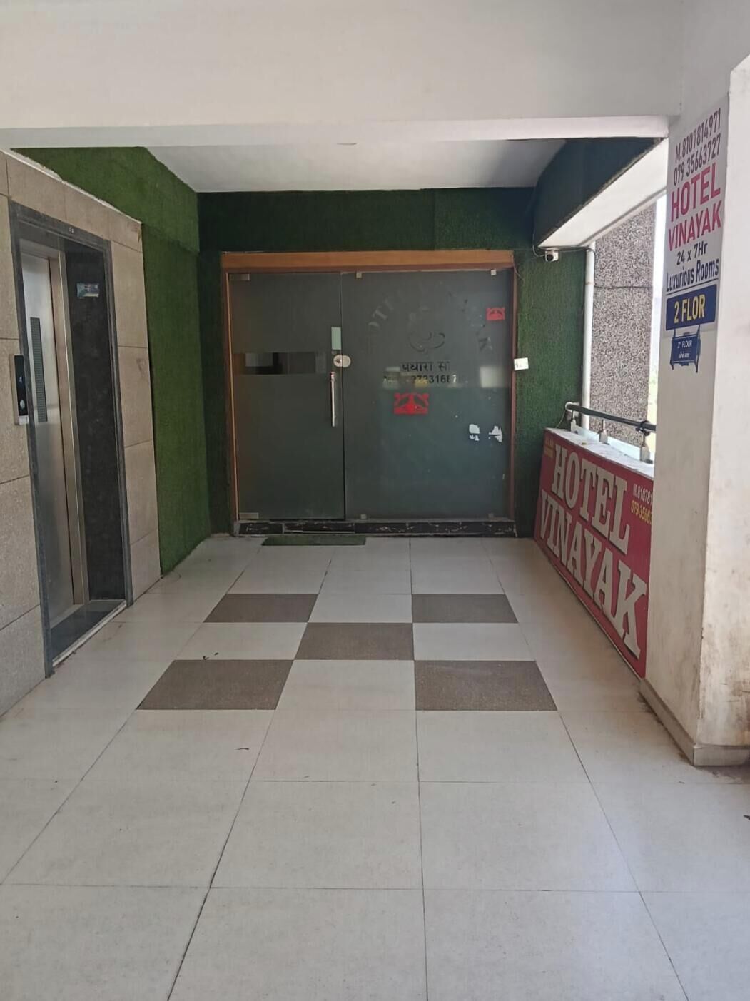 Entrada de hotel con mostrador de recepción, puerta de cristal y un ascensor.