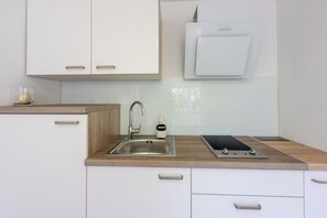A modern kitchen with white cabinets, a stainless steel sink, a built-in oven, and a wooden countertop. - Beautiful apartment in a location very close to the beach (Dramalj)