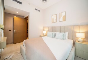 A hotel room with a large bed, bedside lamps, a wooden door, and two wall-mounted artworks. - Luxury 1BR in Business Bay (Dubai)